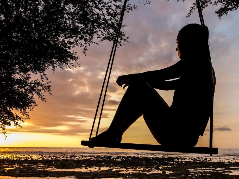 An image of a woman enjoying the view of a sunset while sitting on a swing, immersed in the beauty of the moment.